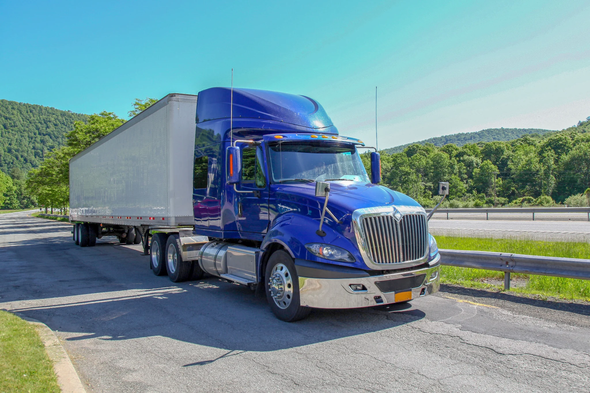 Blue tractor-trailer positioned near a highway